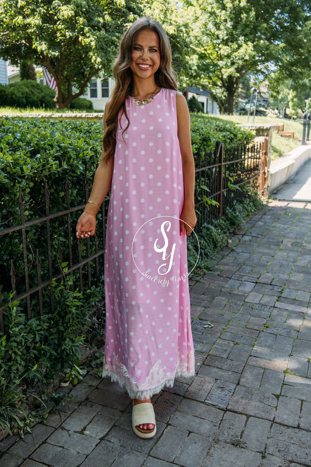 Woman wearing a pink polka dot dress with lace trim on a sidewalk.