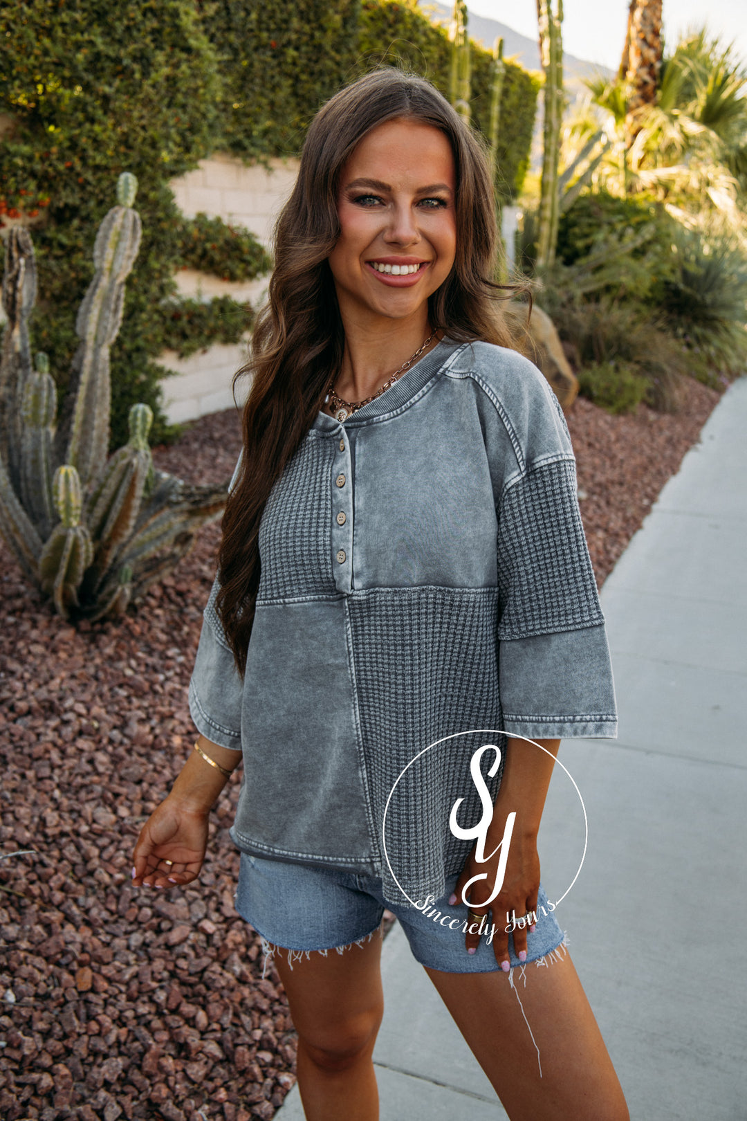 Woman wearing a charcoal top with denim shorts with cacti in the background