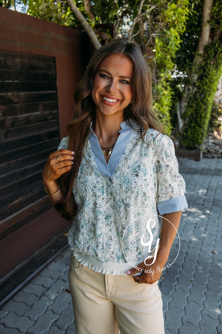 Woman wearing a floral blouse with rolled-up sleeves and beige pants outdoors.
