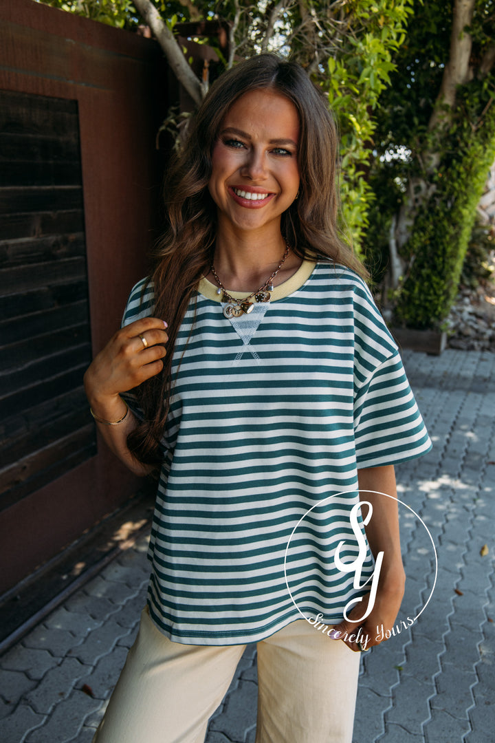 Woman wearing a green and white striped shirt with yellow pants, standing outdoors.