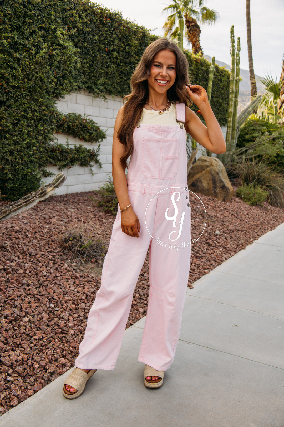 Woman wearing a light pink overalls with a logo on a sidewalk.