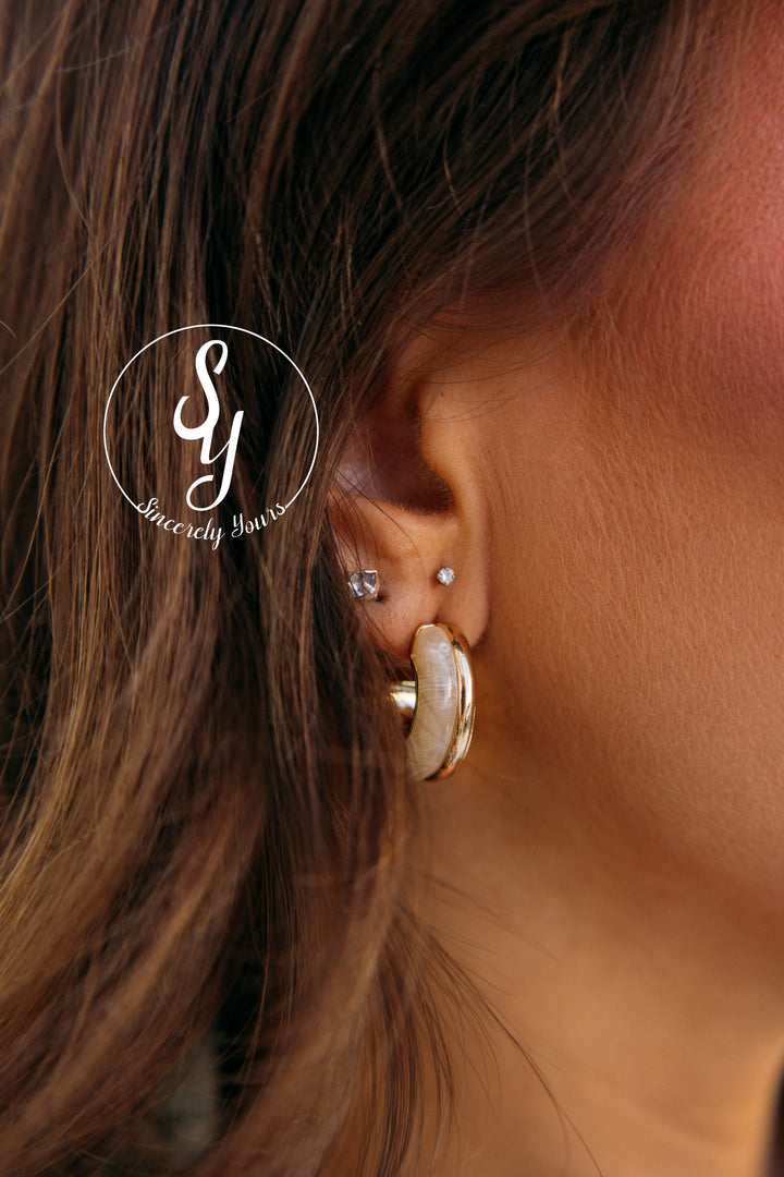 Close-up of an ear wearing gold hoop earrings with a blurred background