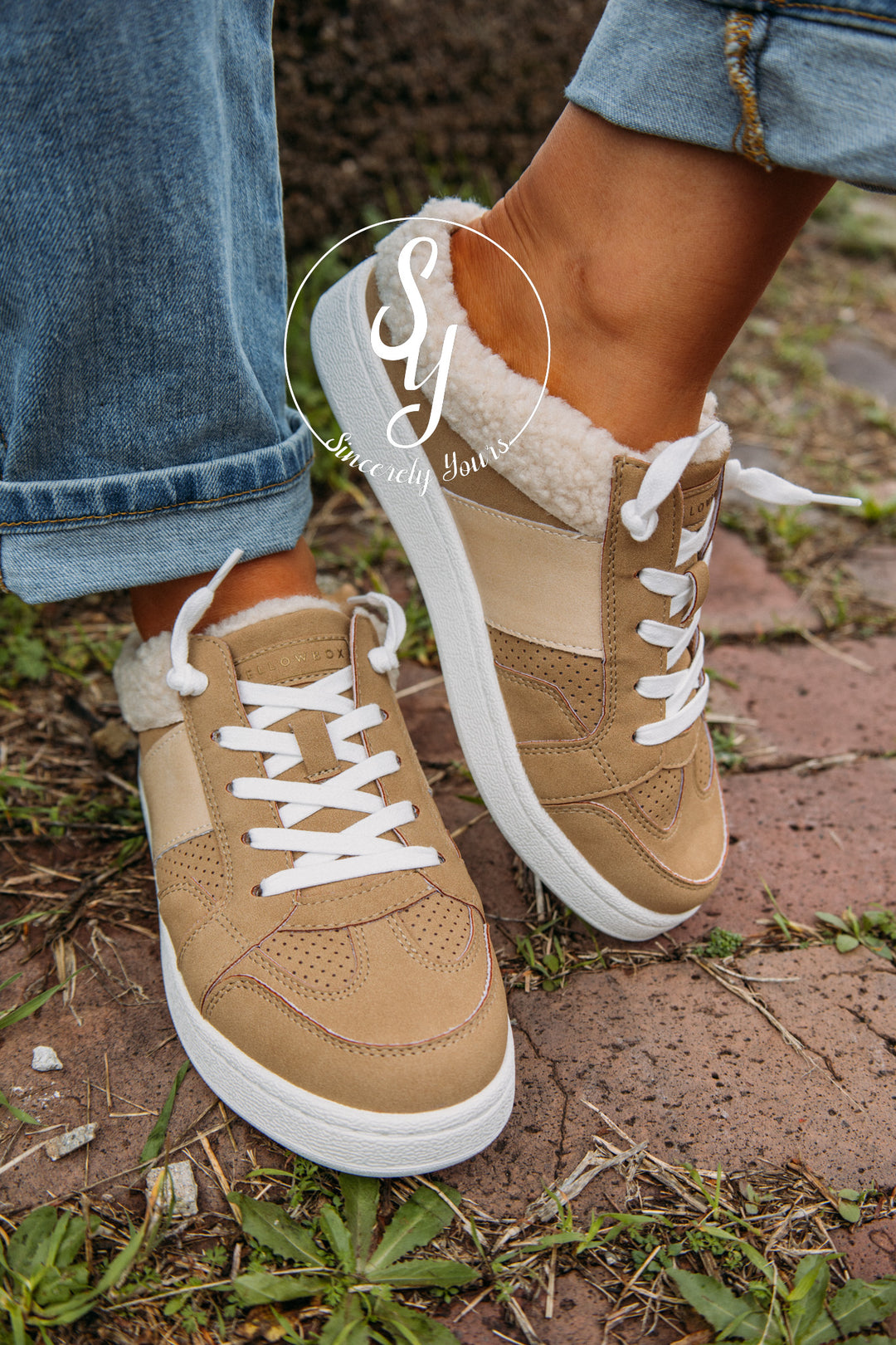 Tan sneakers with white laces worn outdoors on a grassy patch.