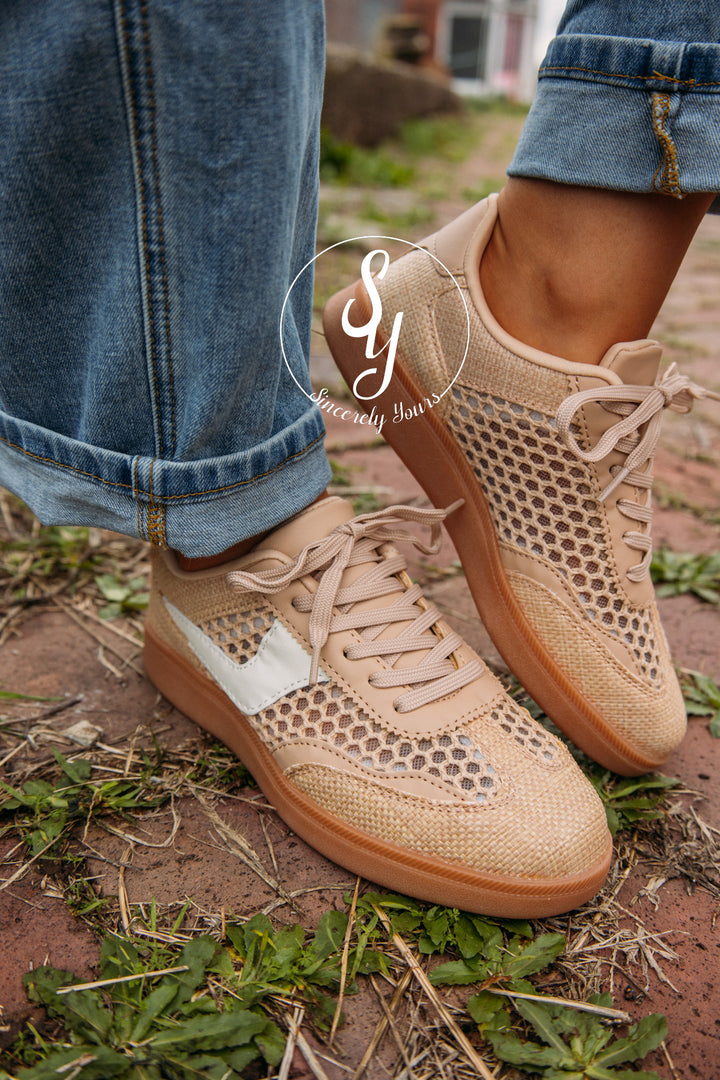 Beige sneakers with mesh design worn outdoors on a person wearing blue jeans.