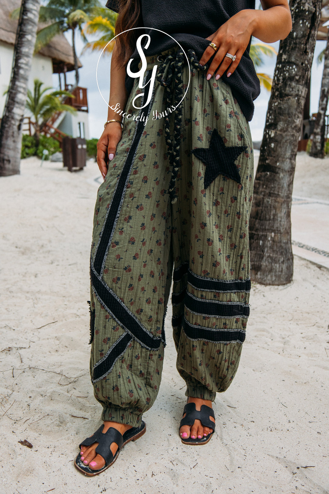 Person wearing patterned pants with star design on a sandy beach with palm trees.
