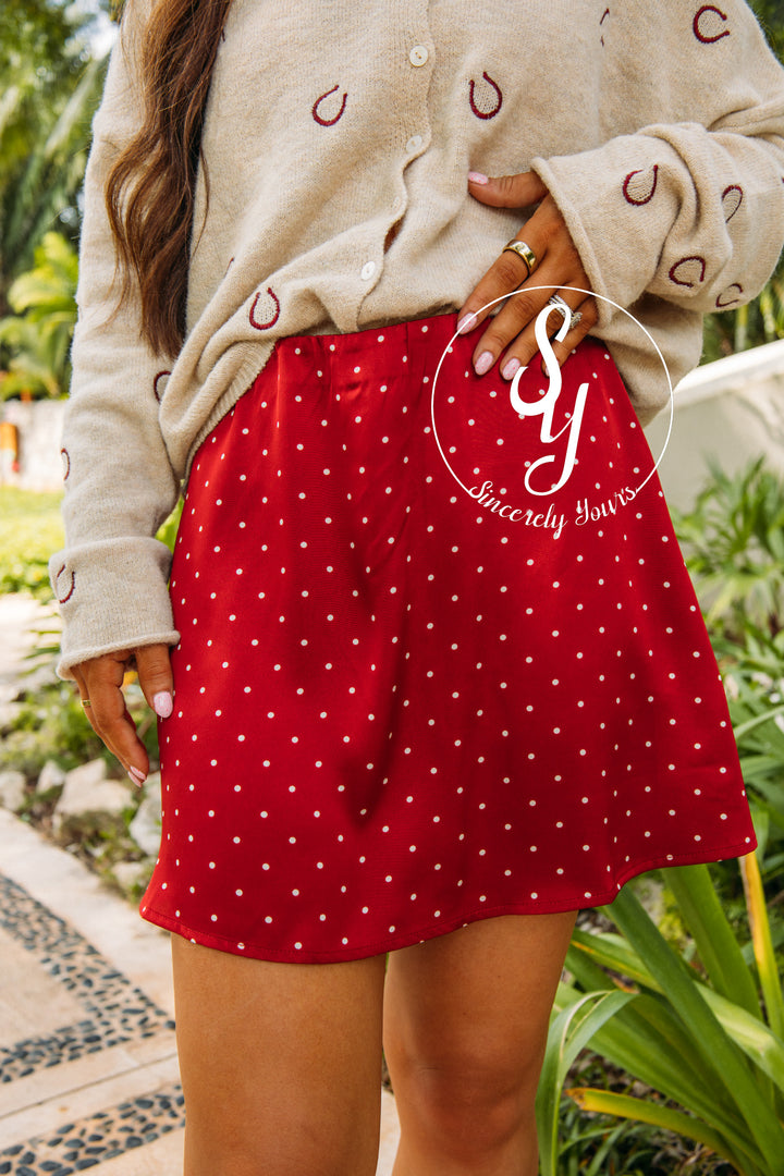 Person wearing a beige cardigan with red polka dot shorts in an outdoor setting