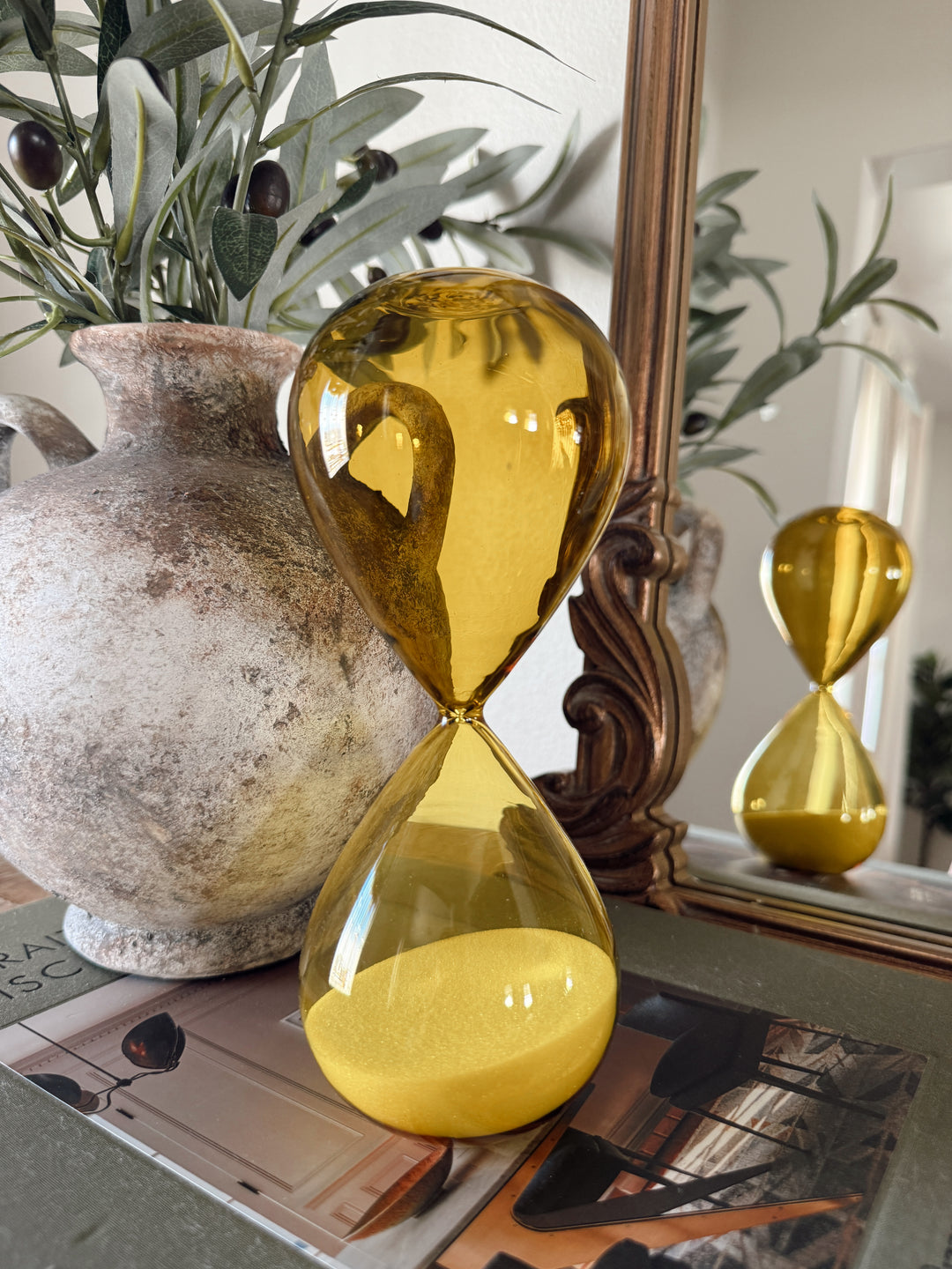 Gold hourglass with sand on a surface with decorative items in the background