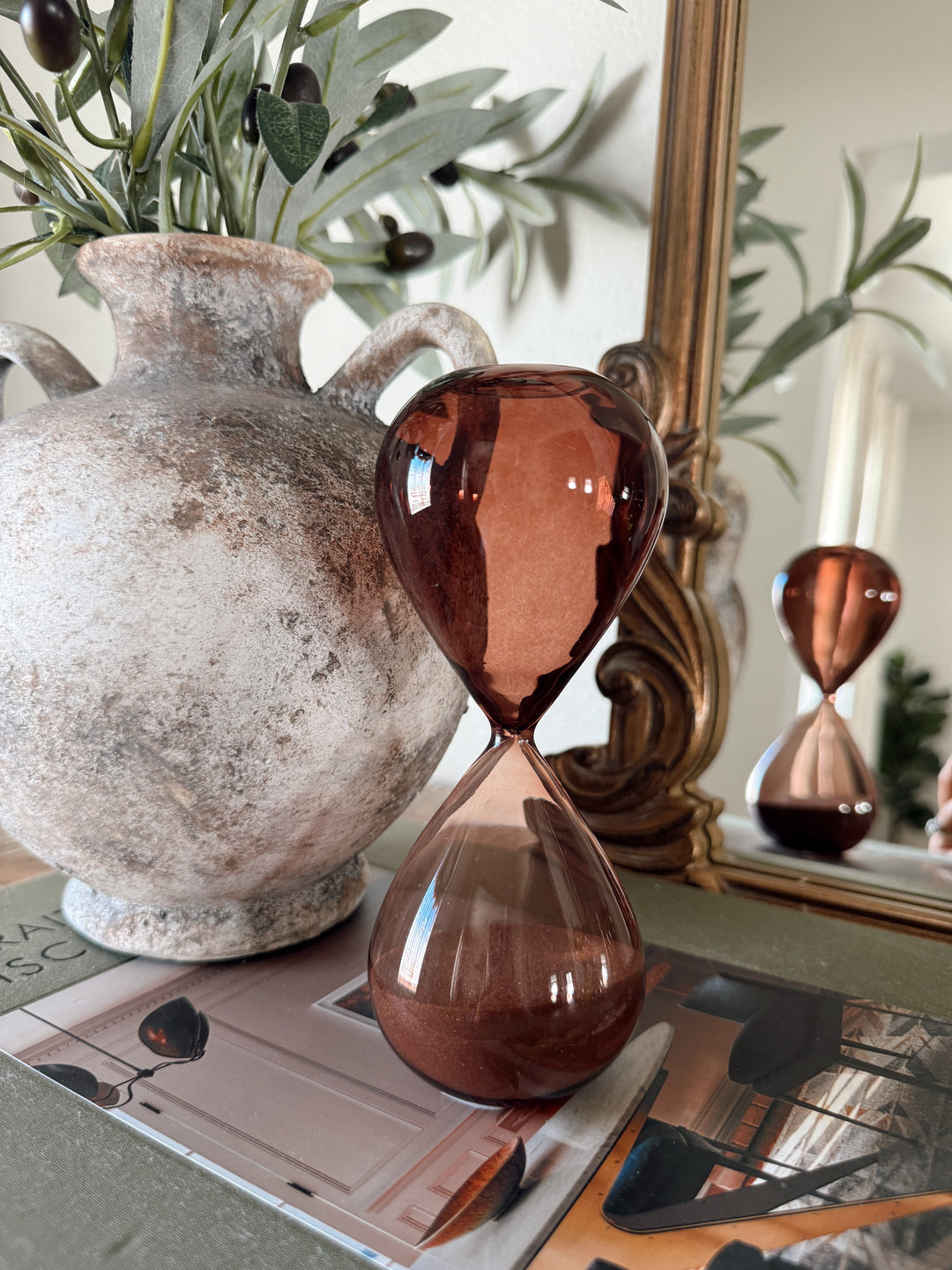Amber hourglass on a surface with a decorative vase and mirror in the background