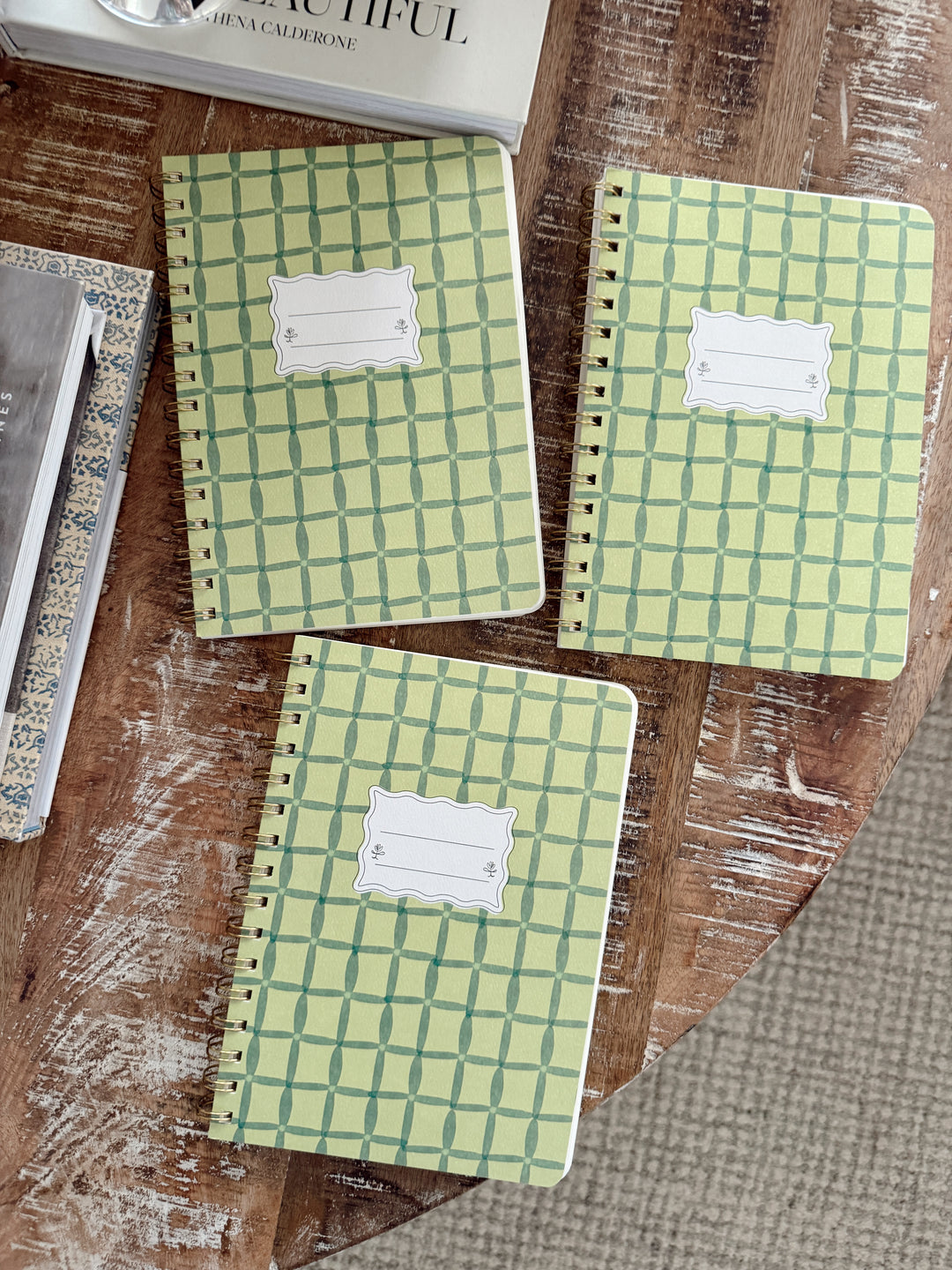 Three green checkered notebooks with labels on a wooden surface