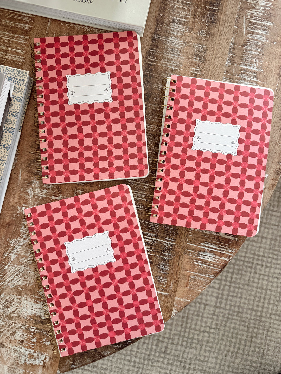 Three red/pink patterned notebooks on a wooden surface