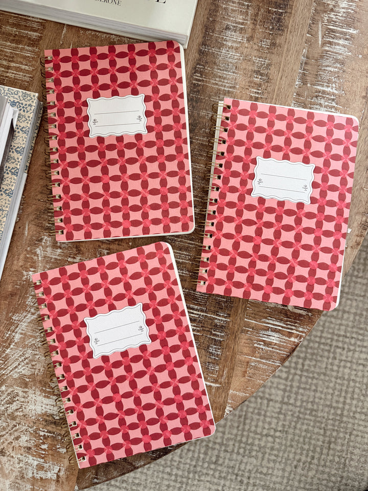 Three red/pink patterned notebooks on a wooden surface